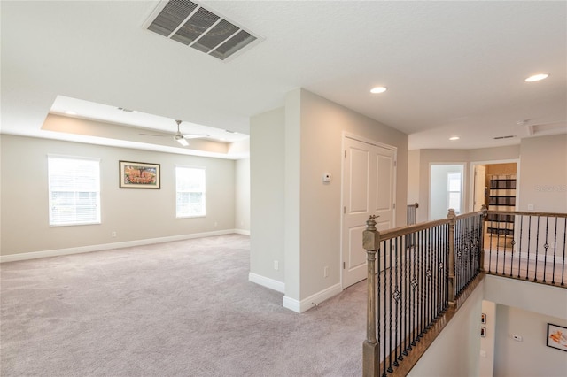 hall featuring a tray ceiling and light colored carpet