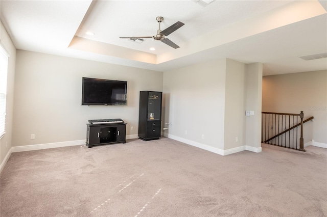 unfurnished living room with a tray ceiling, ceiling fan, and light colored carpet