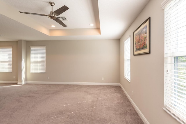 carpeted spare room with a raised ceiling and ceiling fan