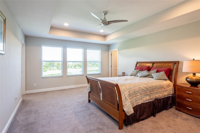 bedroom with a raised ceiling, ceiling fan, and light carpet