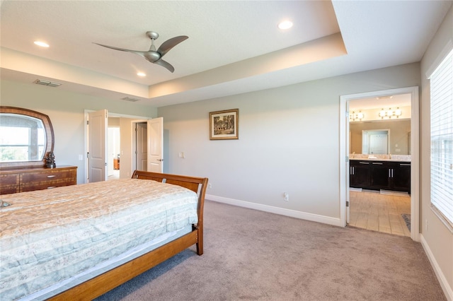 carpeted bedroom with multiple windows, a tray ceiling, ensuite bath, and ceiling fan