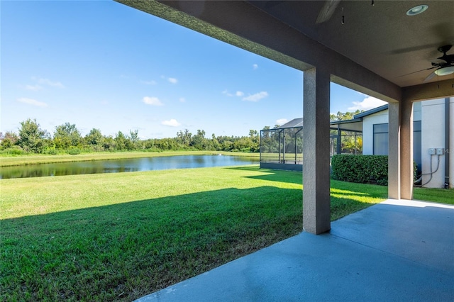 view of yard featuring a patio, a water view, glass enclosure, and ceiling fan