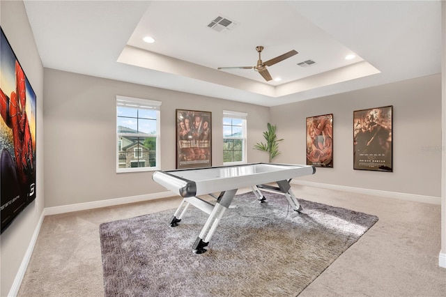 game room with a tray ceiling, light carpet, visible vents, and baseboards