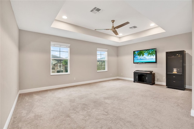 unfurnished living room featuring a tray ceiling, light carpet, visible vents, and baseboards