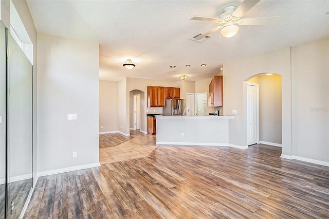 unfurnished living room with a textured ceiling, ceiling fan, and light hardwood / wood-style floors