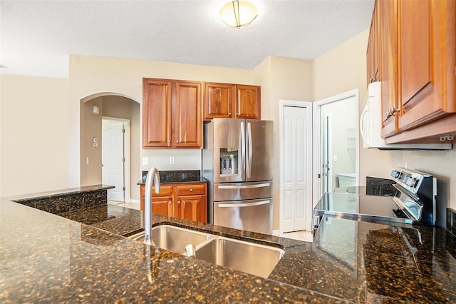 kitchen with sink, a textured ceiling, dark stone counters, and appliances with stainless steel finishes