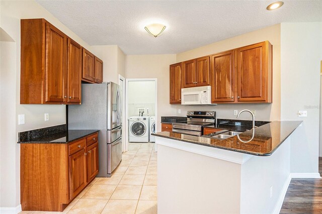 kitchen featuring sink, appliances with stainless steel finishes, washing machine and dryer, kitchen peninsula, and dark stone counters