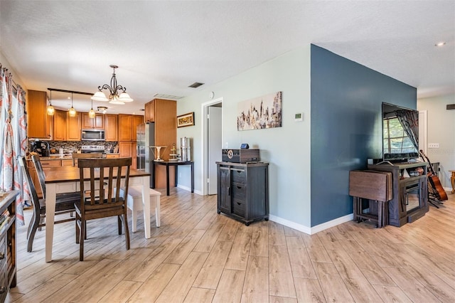 dining room with a textured ceiling, light hardwood / wood-style floors, and a notable chandelier