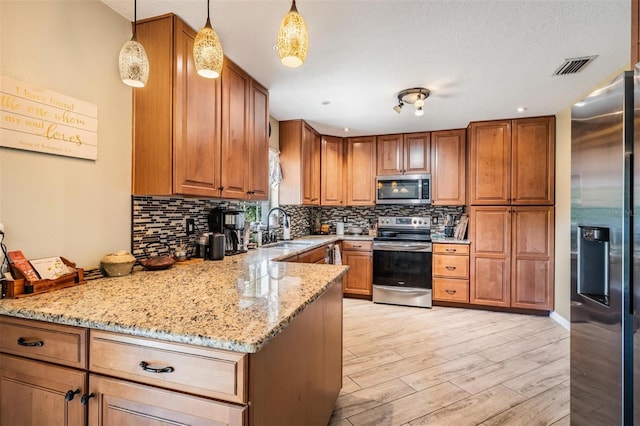 kitchen featuring pendant lighting, appliances with stainless steel finishes, sink, kitchen peninsula, and light stone counters