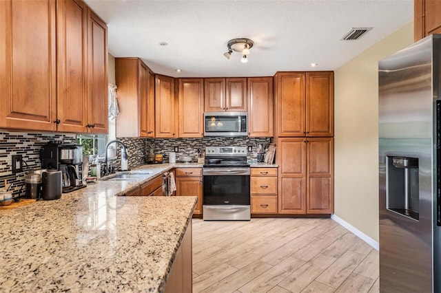 kitchen with tasteful backsplash, sink, light wood-type flooring, light stone countertops, and appliances with stainless steel finishes