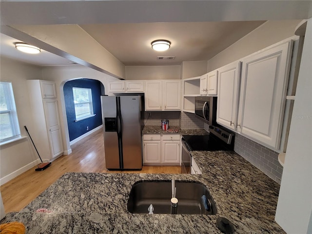 kitchen featuring stainless steel appliances, sink, white cabinetry, decorative backsplash, and dark stone counters