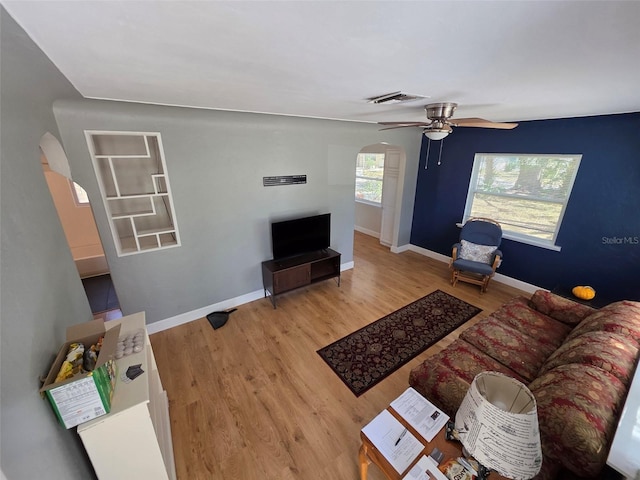 living area with arched walkways, visible vents, a ceiling fan, wood finished floors, and baseboards