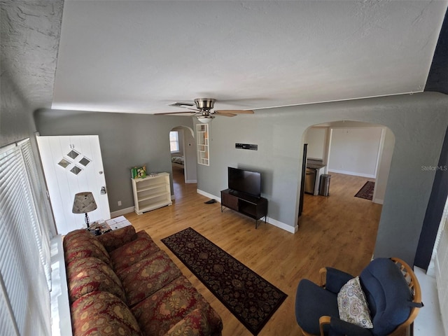 living room with baseboards, light wood-style flooring, arched walkways, and a ceiling fan