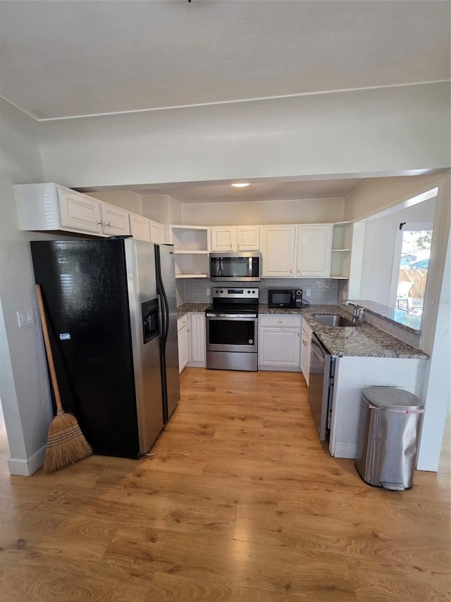 kitchen featuring light wood finished floors, open shelves, stainless steel appliances, decorative backsplash, and a sink