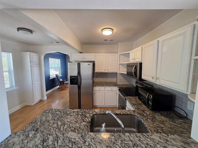 kitchen with arched walkways, a sink, visible vents, appliances with stainless steel finishes, and dark stone countertops