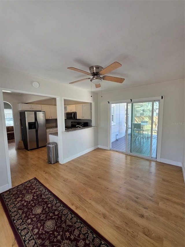 unfurnished living room featuring light wood-style floors, arched walkways, baseboards, and a ceiling fan