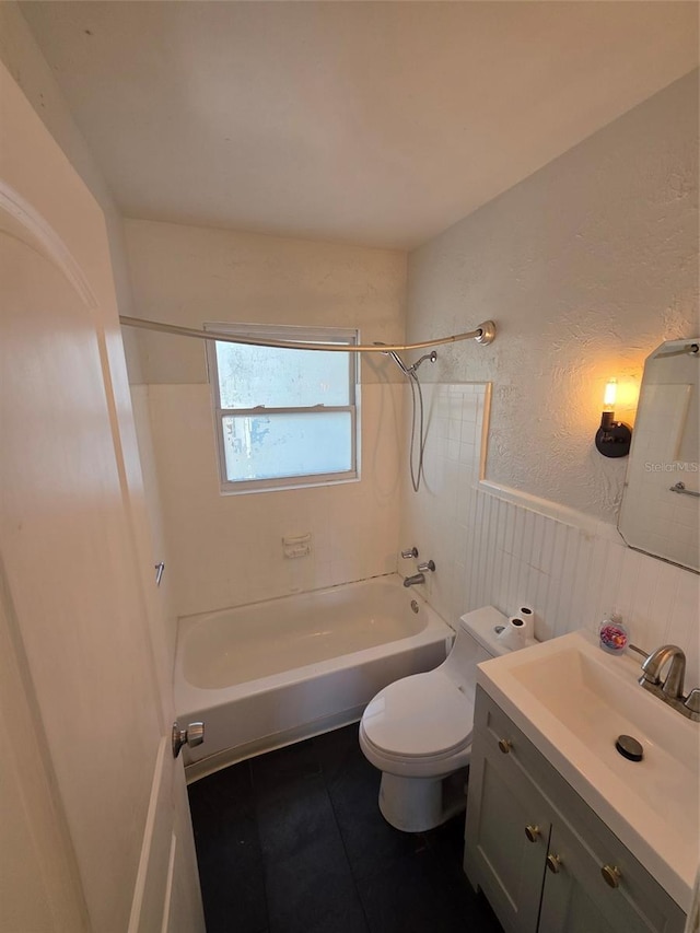 bathroom featuring toilet, vanity, wainscoting, tile patterned floors, and washtub / shower combination