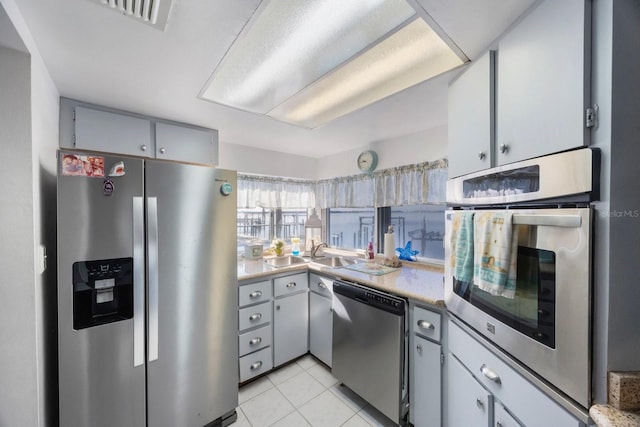 kitchen featuring light tile patterned floors, stainless steel appliances, gray cabinetry, and sink