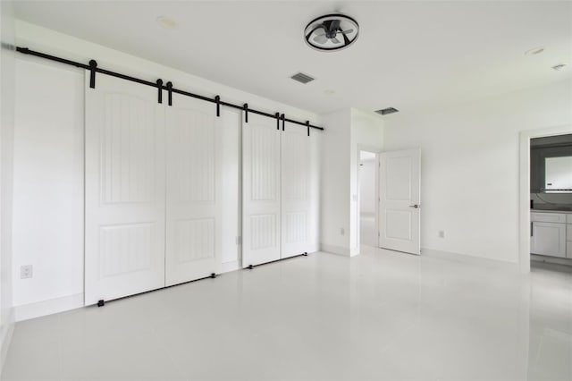 unfurnished bedroom featuring connected bathroom, a closet, light tile patterned floors, and a barn door