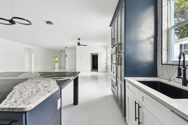 kitchen featuring ceiling fan, a healthy amount of sunlight, light stone counters, and sink