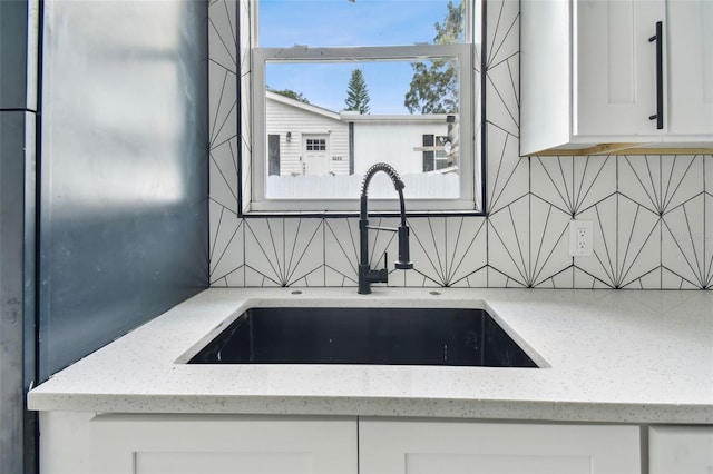 interior details featuring light stone counters, sink, and white cabinets