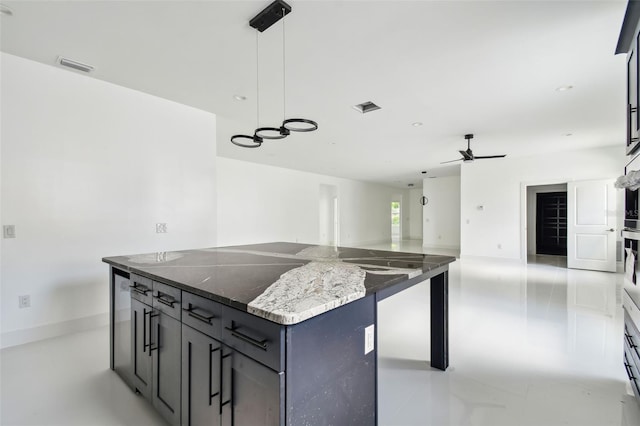 kitchen featuring pendant lighting, a kitchen island, ceiling fan, and dark stone countertops