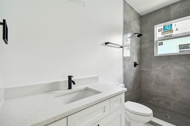 bathroom with a tile shower, vanity, and toilet