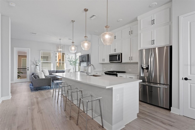 kitchen with white cabinets, appliances with stainless steel finishes, a kitchen island with sink, and hanging light fixtures