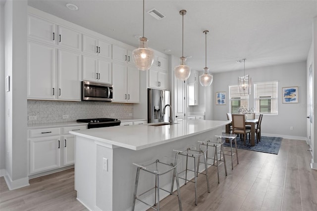 kitchen with white cabinetry, a kitchen island with sink, tasteful backsplash, and appliances with stainless steel finishes