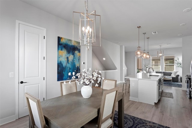 dining space with a chandelier, light wood-type flooring, and sink