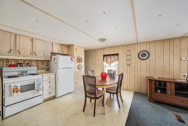 kitchen featuring white appliances, wooden walls, a textured ceiling, and light brown cabinets