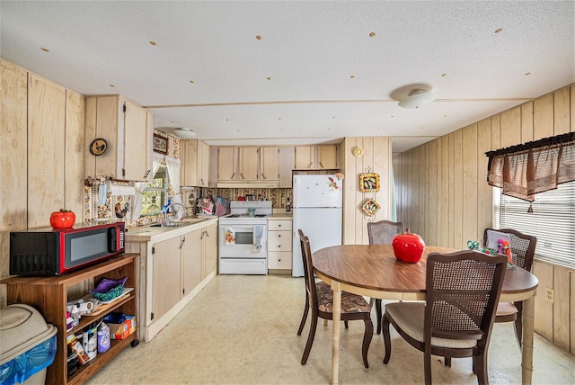 kitchen featuring sink, wooden walls, a textured ceiling, light brown cabinets, and white appliances