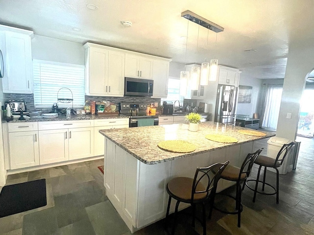 kitchen featuring pendant lighting, a kitchen island, white cabinetry, stainless steel appliances, and a breakfast bar