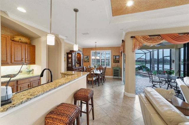 kitchen featuring a kitchen breakfast bar, light stone counters, crown molding, decorative light fixtures, and a water view