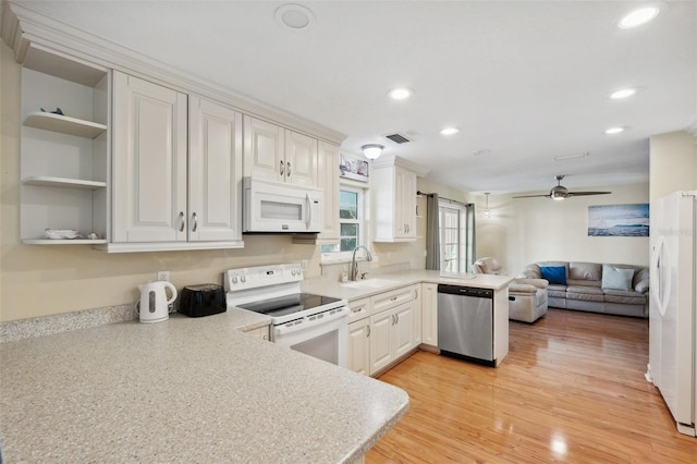 kitchen with white appliances, light wood-type flooring, kitchen peninsula, white cabinets, and sink