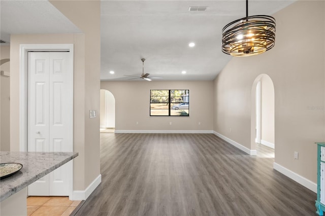 unfurnished living room featuring ceiling fan with notable chandelier and wood-type flooring