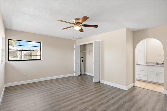 unfurnished bedroom with a closet, connected bathroom, light wood-type flooring, ceiling fan, and sink