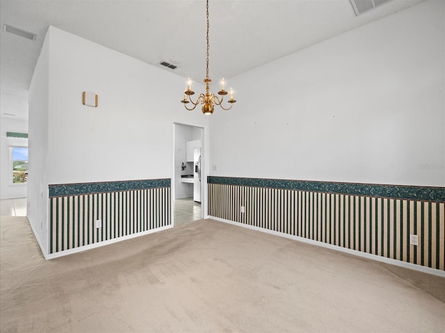 unfurnished room with a notable chandelier, vaulted ceiling, and carpet flooring