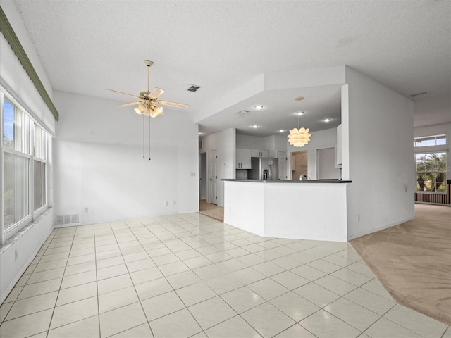 unfurnished living room featuring a textured ceiling, light tile patterned flooring, and ceiling fan with notable chandelier