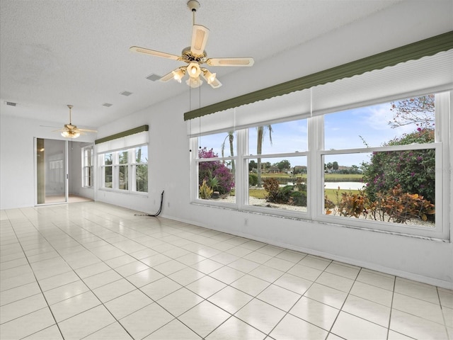 tiled empty room with a textured ceiling, ceiling fan, and a water view