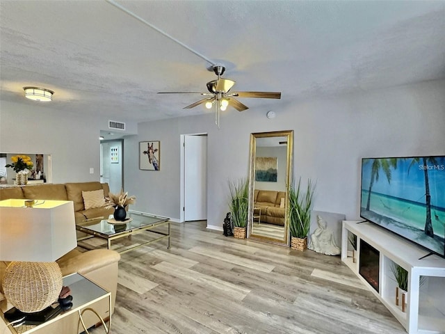 living room with ceiling fan, a textured ceiling, and light wood-type flooring