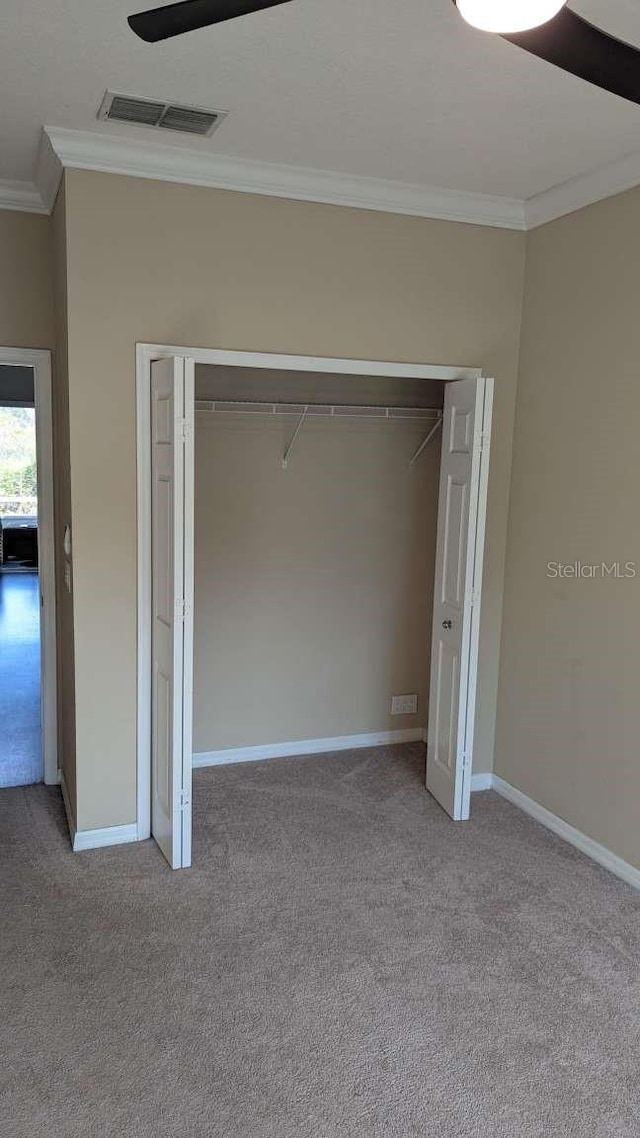 unfurnished bedroom featuring ceiling fan, a closet, light colored carpet, and ornamental molding