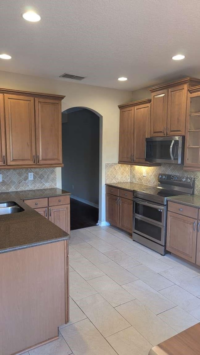 kitchen featuring sink, a textured ceiling, appliances with stainless steel finishes, tasteful backsplash, and light tile patterned flooring