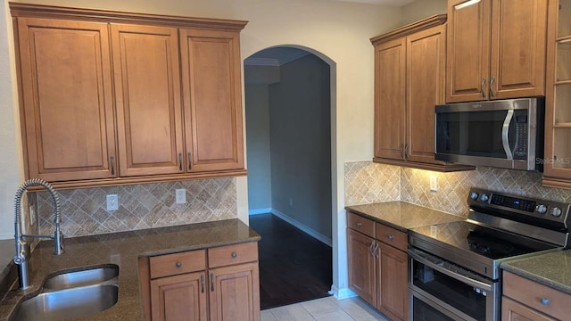 kitchen featuring stainless steel appliances, tasteful backsplash, dark stone counters, and sink