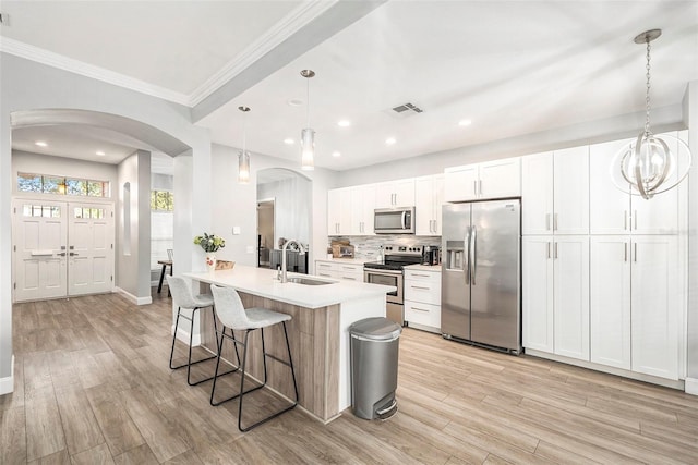 kitchen with pendant lighting, sink, appliances with stainless steel finishes, an island with sink, and white cabinets