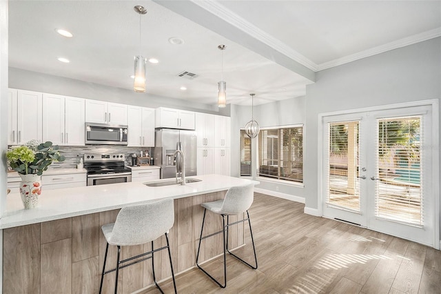 kitchen featuring white cabinetry, light hardwood / wood-style floors, stainless steel appliances, pendant lighting, and sink