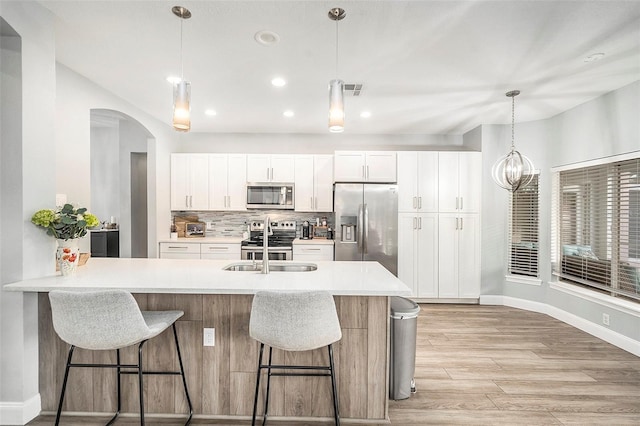 kitchen featuring appliances with stainless steel finishes, decorative light fixtures, white cabinetry, backsplash, and a breakfast bar