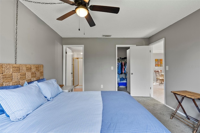 bedroom with connected bathroom, a walk in closet, light colored carpet, ceiling fan, and a closet