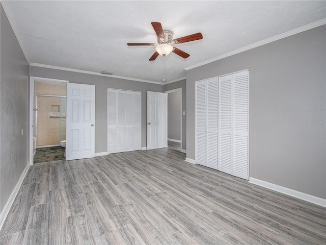 unfurnished bedroom featuring ceiling fan, ensuite bathroom, crown molding, and multiple closets