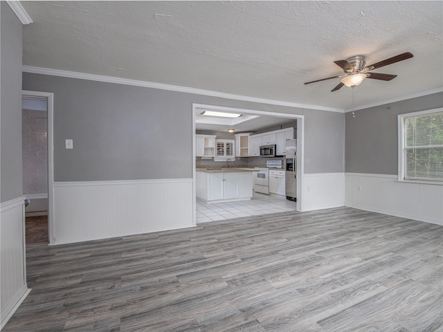 unfurnished living room with crown molding, a textured ceiling, sink, light hardwood / wood-style flooring, and ceiling fan